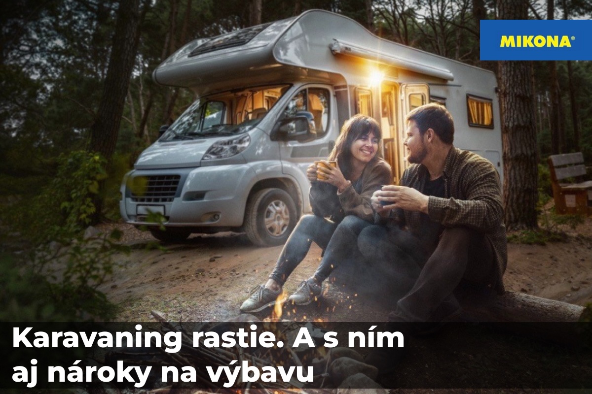 Karavan zaparkovaný v lese pri večernom kempovaní, pár sediaci pri ohni pred obytným vozidlom počas cestovania karavanom